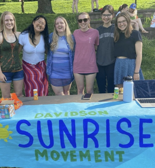 a group of students standing behind a table with a sign that reads " Sunrise Movement"