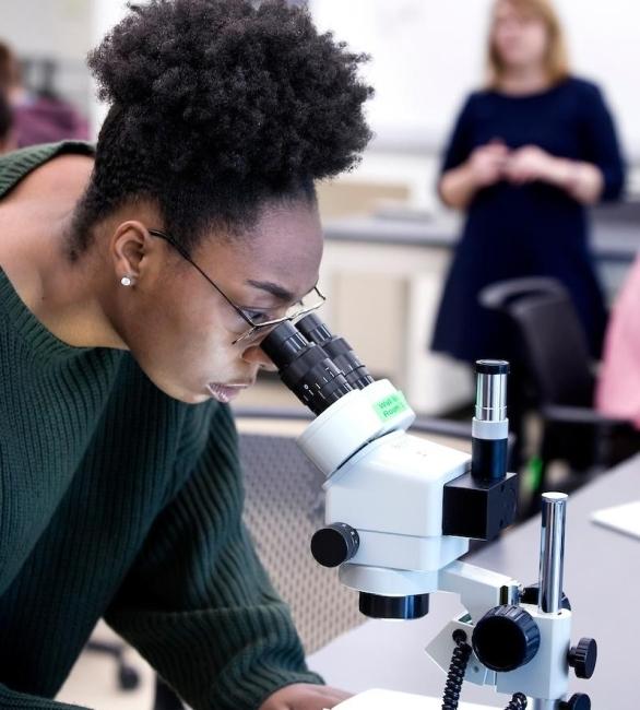 Student looking through a microscope with professor in the background