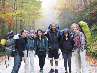 Students backpack with camping gear in the mountains with fall foliage 