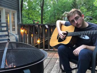  College music scholarship student Cooper Ray Oljeski '25 holds guitar on patio with firepit