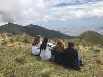 Backs of 4  students sitting down, looking at scenic mountain view in Ecuador